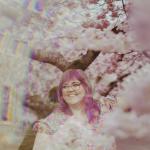 White cis female therapist of large body surrounded by cherry blossom trees in bloom.
