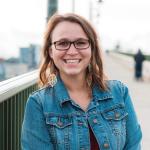 Photo of Maggie Hemphill smiling in a jean jacket with a bridge in the background. 